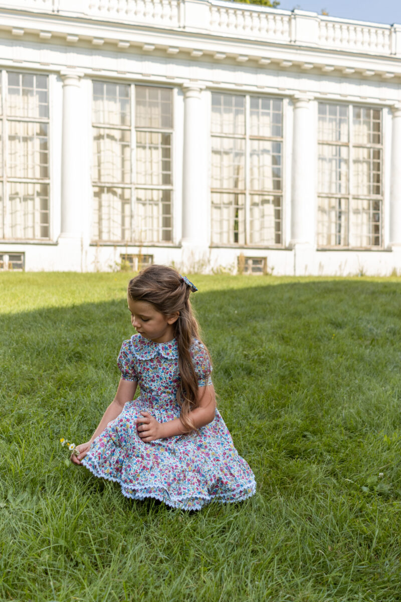 girl sitting on a grass in a dress with ruffles and white lace liberty print