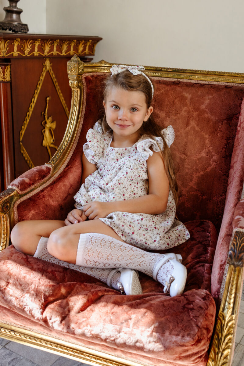 girl sitting on a chair in white dress and headband and white socks