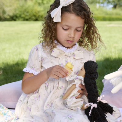 girl wearing floral dress bridgerton inspired on a picnic with her doll