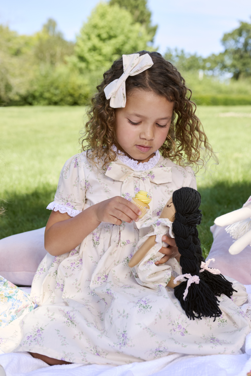 girl wearing floral dress bridgerton inspired on a picnic with her doll