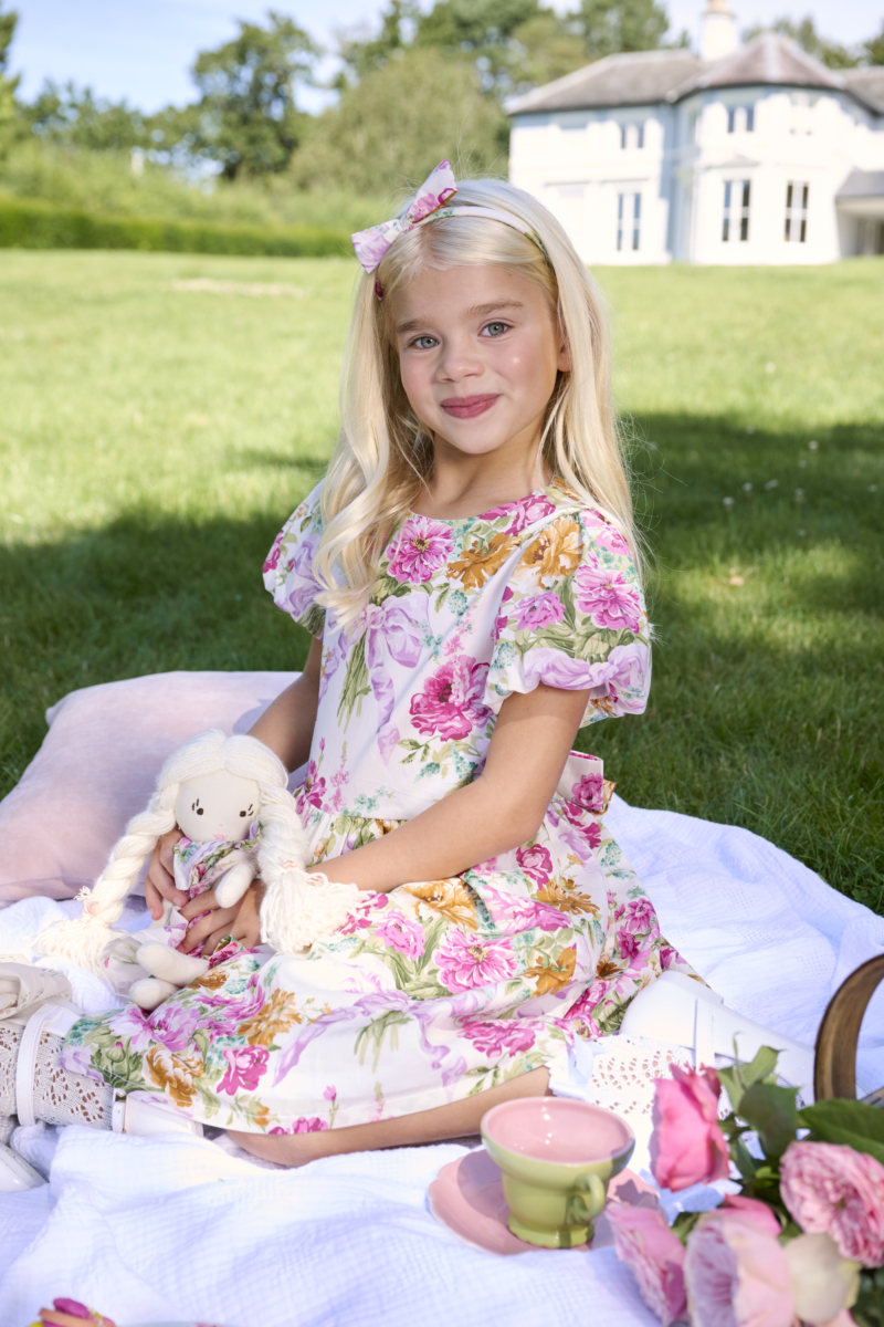 girl sitting on picnic with her doll in floral dress bridgerton inspired